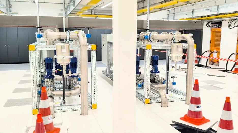 Cooling infrastructure under construction at Leeghwater, Aalsmeer: two pump skids with stainless-steel coolant pipework on a raised data-hall floor, marked off with traffic cones
